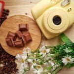 instant photo camera near chocolate and spilled coffee beans indoors